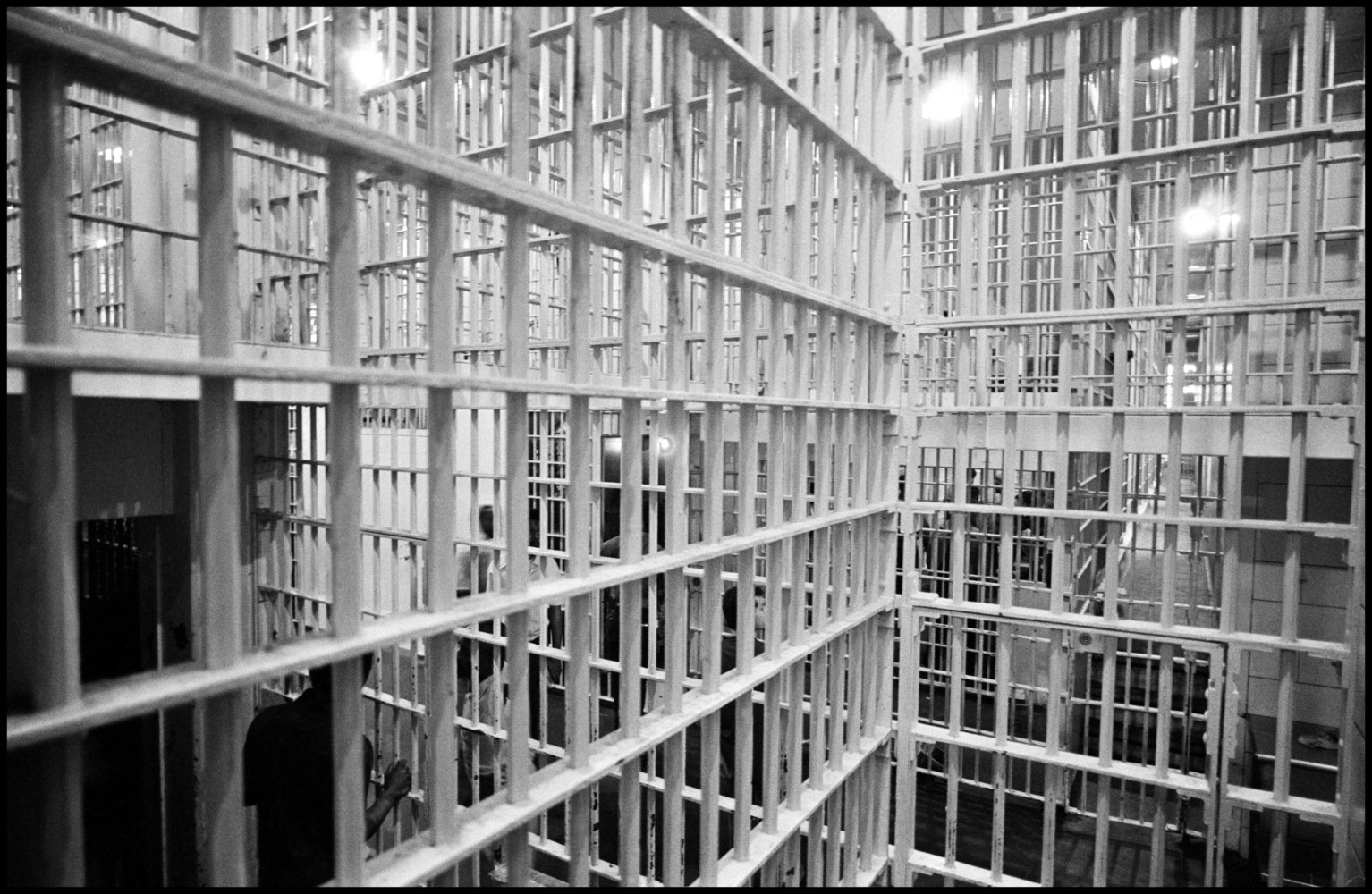Black and white photograph from inside a jail cell. White bars overlapping. 